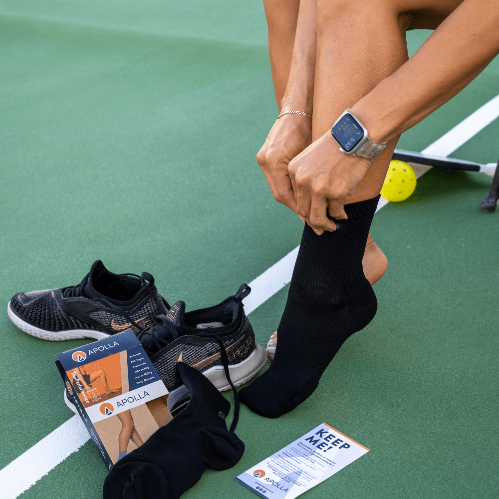 Woman putting on crew socks for foot pain relief on pickleball court