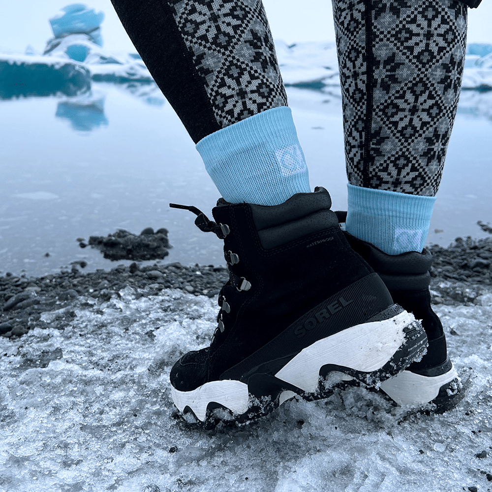 Powder blue crew socks with ankle support worn by woman hiking a glacier