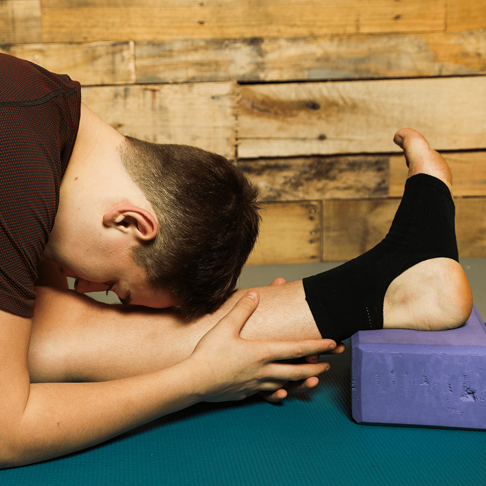 Black ankle brace worn by man as ankle compression sleeve while doing yoga