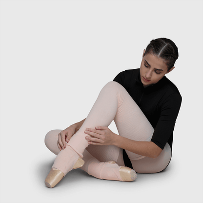 Ballerina putting on pink dance leg warmers with knee support