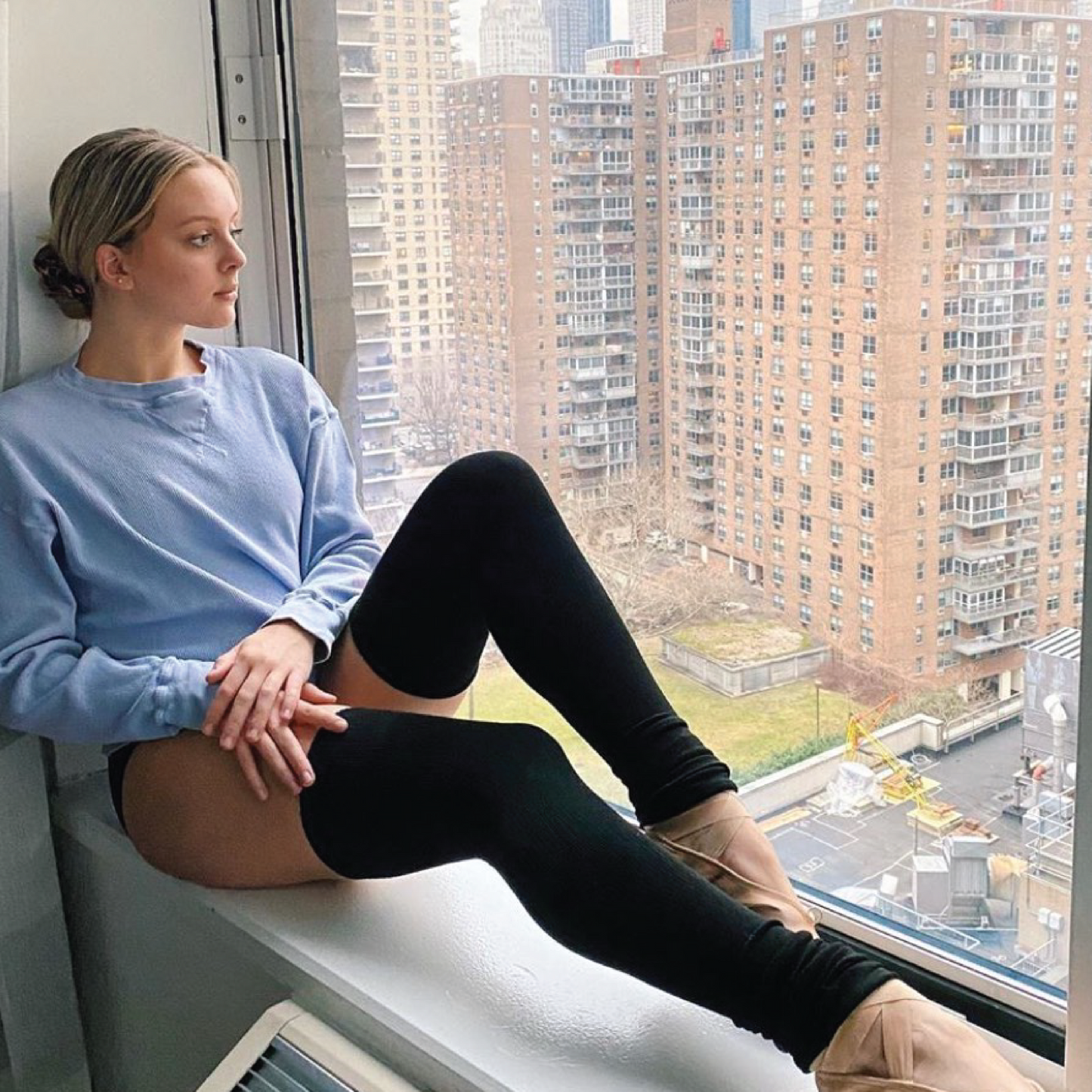 Ballerina wearing dance leg warmers with knee support looking out a studio window